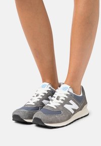 Grå och marinblå New Balance-sneakers med vita detaljer. Har mesh- och mockamaterial, snörning och en strukturerad gummisula.