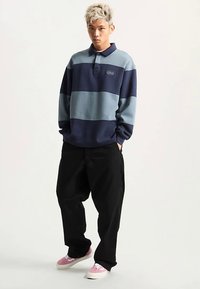 Granatowo-niebieski pulower w paski z kołnierzykiem, z małym logo. Do tego luźne czarne spodnie i różowe trampki.