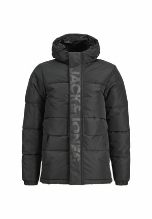 Czarna pikowana kurtka z kapturem, noszona na granatowej koszuli z białym napisem, w połączeniu z luźnymi oliwkowymi spodniami i czarnymi trampkami.