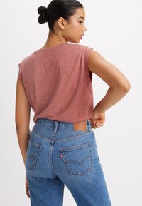 Rode heidelook mouwloze shirt gecombineerd met high-waisted blauwe denim jeans met een leren patch en zichtbare achterzakken.