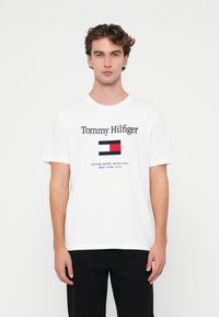 Hvid bomulds T-shirt med "Tommy Hilfiger" logo og flag grafik i rød, blå og hvid. Korte ærmer og rund hals design.