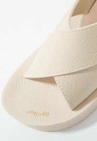 Sandales beige clair avec un motif texturé semblable à celui des reptiles sur la bride supérieure. Semelle épaisse pour plus de confort. Marque embossée sur la semelle.