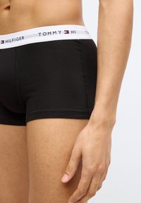 Μαύρα βαμβακερά ανδρικά εσώρουχα boxer με λευκή ζώνη μέσης που φέρει το "TOMMY HILFIGER" και λογότυπα. Λείο ύφασμα, εφαρμοστό σχέδιο.