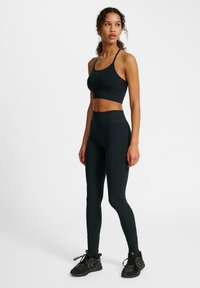 Zwarte sportset bestaande uit een aansluitende bh-top met dunne bandjes en hooggeknoopte legging. Beide stukken zijn gemaakt van gladde, rekbare stof.