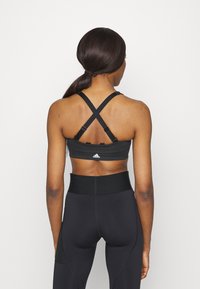 Sutiã desportivo preto com alças cruzadas, apresentando um pequeno logotipo na parte de trás. Combinado com leggings pretas de cintura alta. Textura suave.