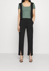 Grön randig kortärmad topp med fyrkantig halsringning, kombinerad med högmidjade svarta byxor med sidoflikar, bärs med svarta remsandaler.