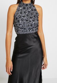 Black satin evening dress featuring a halter neck and a beaded, embroidered bodice with embellishments, providing a structured yet elegant silhouette.