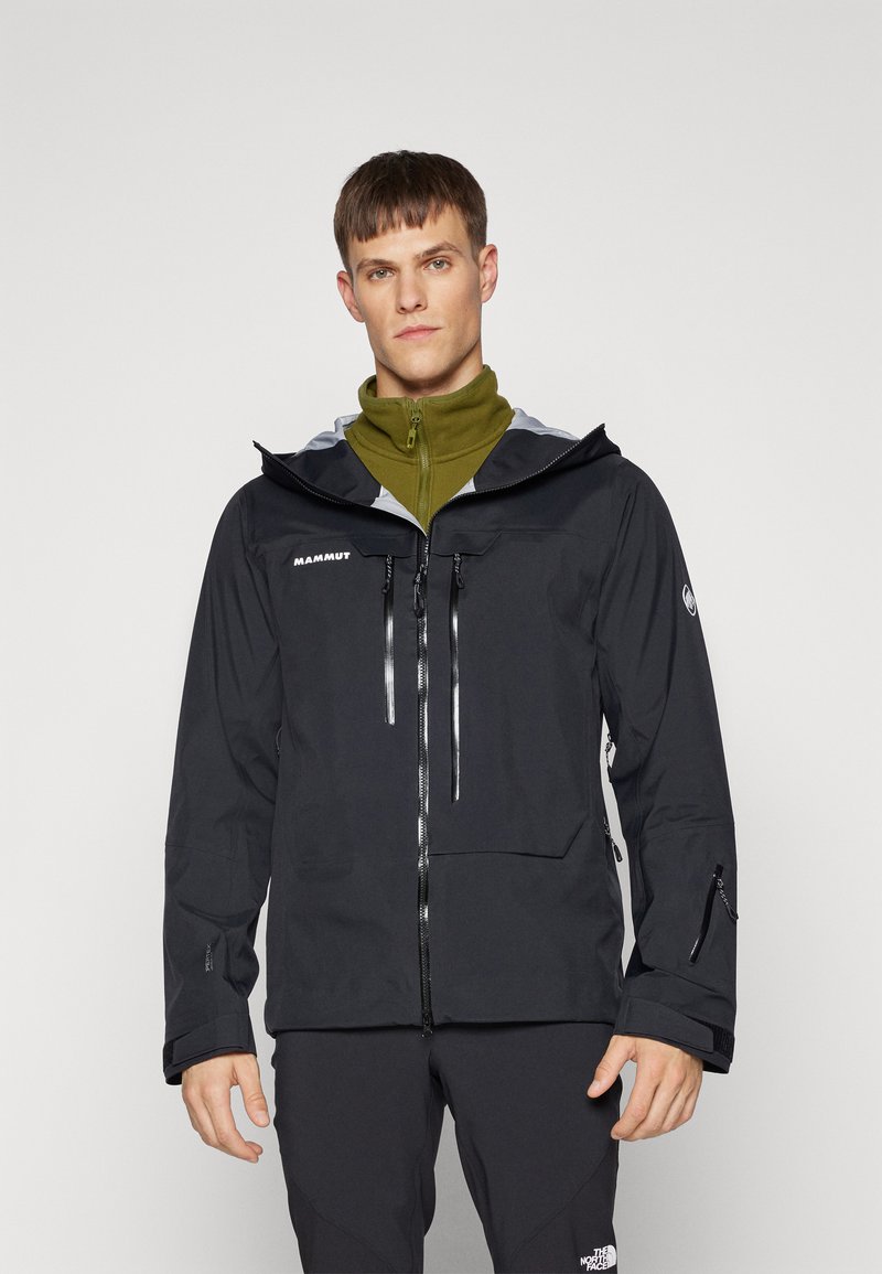 Chubasquero negro impermeable con capucha gris, cierre frontal con cremallera, dos bolsillos frontales con cremallera y puños ajustables, combinado con una capa interna verde.