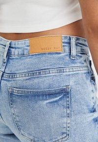 Lichtblauwe denim jeans met een leren label met de tekst "NOISY MAY" op de tailleband. Zichtbare stiksels en klassieke achterzakken.