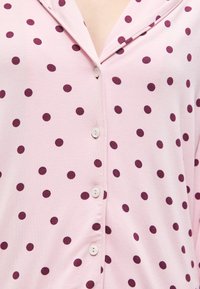 Chemise rose pâle à boutons avec des pois violet foncé et un col à cran, vue de la poitrine au milieu du torse.