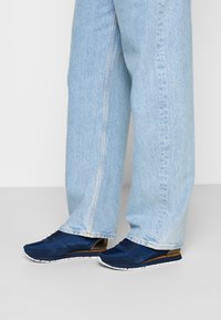 Marine sneakers med en blanding av teksturert stoff og glatte overlag, hvit spraglete såle, kombinert med lyse blå, litt løse jeans.