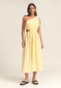 Keltainen, yhden olkapään mekko, jossa joustava vyöt�ärö, sivuleikkaus ja liehuva helma. Rakenteinen kangas, yhdistetty mustiin tasapohjaisiin sandaaleihin.