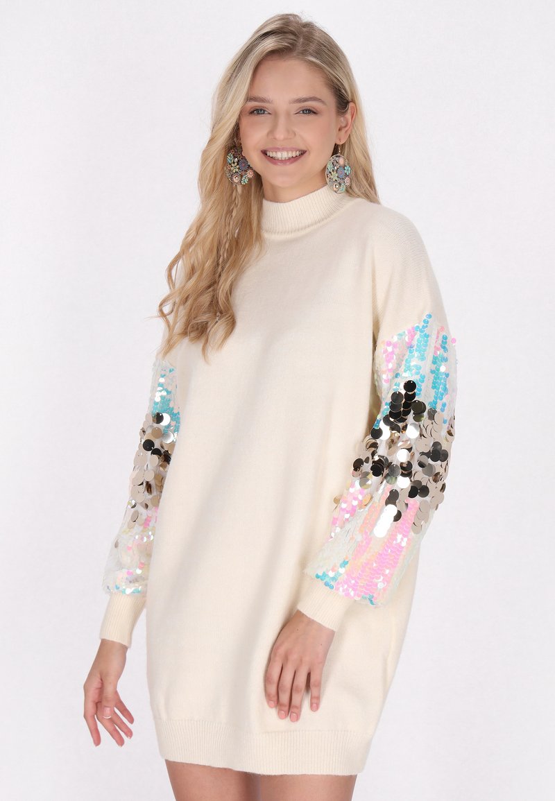 Strickkleid in Creme mit langen Ärmeln, die mit mehrfarbigen Pailletten geschmückt sind, und einem hohen Kragen. Weicher Stoff und lockere Passform.