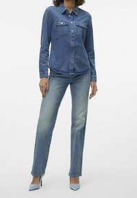 Denim shirt with long sleeves, buttoned front, two chest pockets; paired with faded blue straight-leg jeans; blue high-heeled shoes.