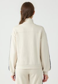 Beige Sweatshirt mit langen Ärmeln und hohem Kragen, gerafften Bündchen und seitlichen Streifen. Glatte Textur mit lockerer Passform und schlichtem Design.