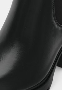 Bottine noire en cuir lisse avec panneau latéral élastique et talon épais, montrée en gros plan.