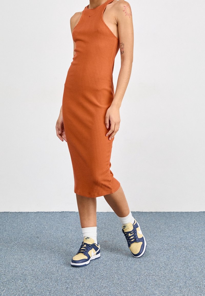 Žebrované midi šaty těsného střihu v barvě spálené oranžové s bezramínkovým designem. Kombinované s námořnickými a žlutými teniskami a bílými ponožkami do půli lýtek.