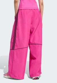 Baggy pink track pants made of lightweight fabric, featuring black accent stripes and side pockets, elastic waistband, and a smooth texture.
