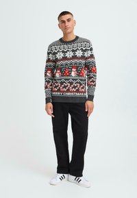 Knit sweater in dark gray with festive patterns featuring snowmen, candy canes, and "MERRY CHRISTMAS" text. Ribbed cuffs and hem.