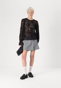Black lace long-sleeve top, houndstooth pleated mini skirt, white knee-high socks, black shoes, and a black handbag.