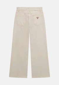 Jean beige à jambes larges en coton, avec deux poches arrière ornées d'un logo triangulaire. Texture lisse et coutures soignées.