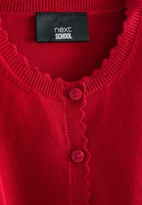 Czerwony dziergany sweter z krawędziami w kształcie fali, dwoma czerwonymi guzikami i czarną etykietą "next SCHOOL" wewnątrz kołnierza.