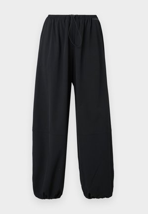 Pantalons noirs à taille élastique avec cordon de serrage, présentant des jambes fuselées qui se resserrent aux chevilles et deux poches latérales. Fabriqués en matériau doux.