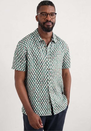 Chemise à manches courtes à carreaux avec des carrés verts, blancs et roses, design à boutons, et une poche poitrine. Tissu en coton avec une texture lisse.