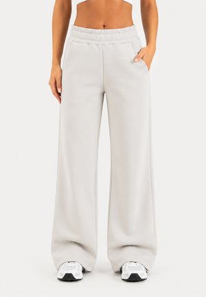 Pantalon de survêtement ample gris clair avec jambes larges, poches latérales et taille élastique, associé à des baskets blanches et noires.