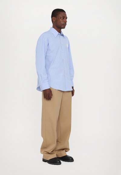 Camisa de botones en azul claro con finas rayas blancas, combinada con pantalones de pierna ancha beige y zapatos gruesos negros.