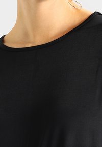 Schwarzes Shirt mit einem breiten, runden Ausschnitt. Glatte Textur und leichtes Material. Keine sichtbaren Muster oder Akzente. Minimalistisches Design.