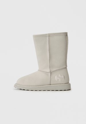 Svetlosivé semišové čižmy po členky s plochou podrážkou a vyšitým logom na vonkajšej päte, zobrazené z bočného profilu na bielom pozadí.