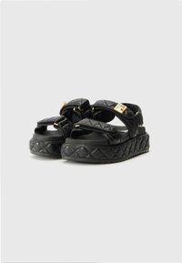 Sandales plateformes noires matelassées avec des sangles ajustables et des accents en métal doré, dotées d'une semelle texturée pour une meilleure adhérence et un confort accru.