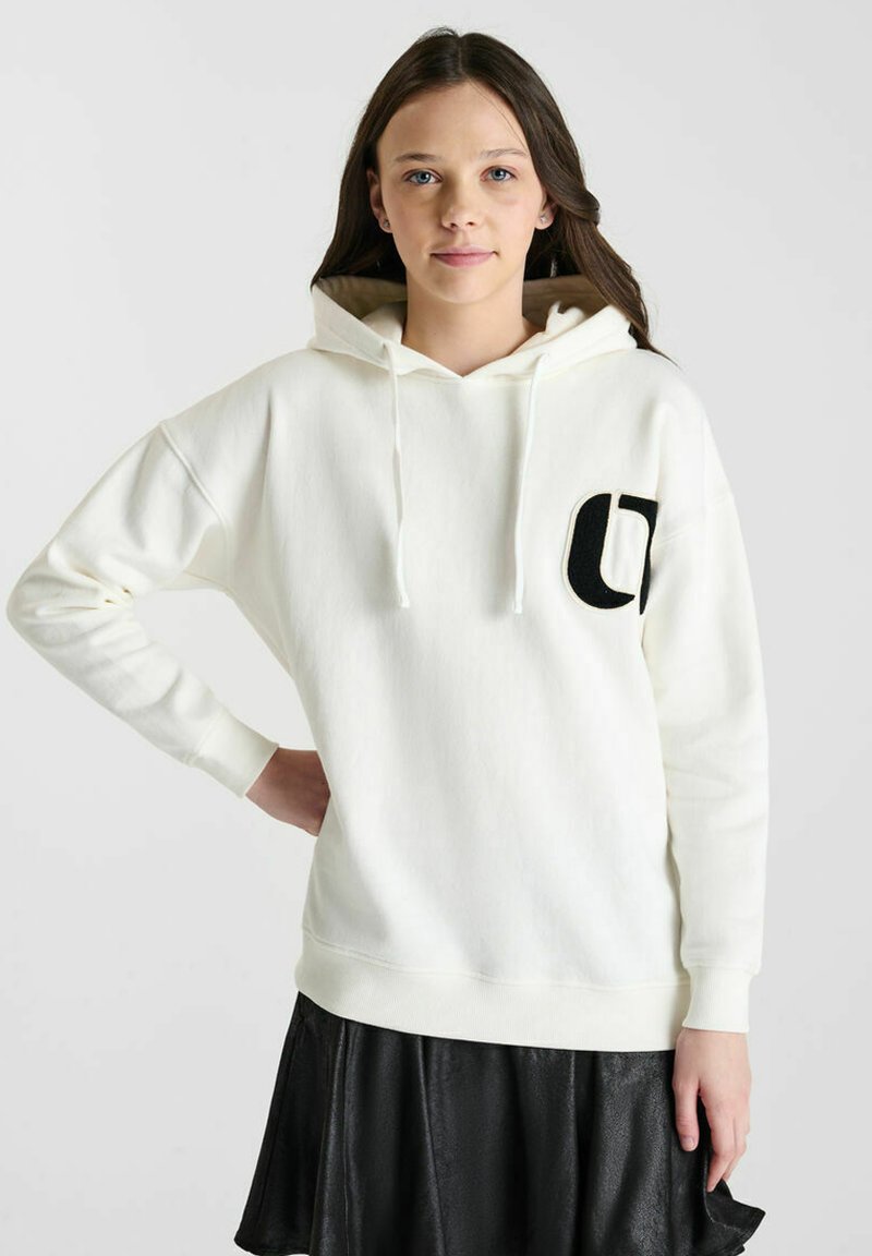 Witte katoenen hoodie met een voorzak, trekkoorden en een groot zwart logo aan de linkerkant, gecombineerd met een zwarte rok. Soepele textuur.