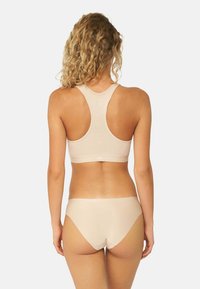 Top sportivo color nude con design a racerback, realizzato in tessuto morbido e con una fascia in vita senza cuciture. Abbinato a slip in stile bikini coordinati.