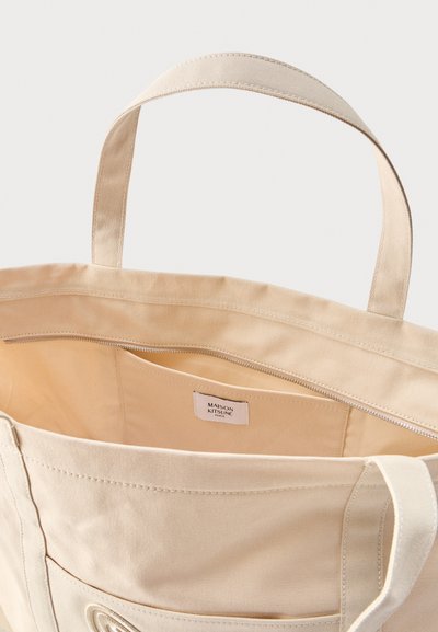 Καμβά τσάντα ώμου σε μπεζ με διπλές λαβές, εσωτερική τσέπη με φερμουάρ και ετικέτα με την επιγραφή "Maison Kitsuné Paris".