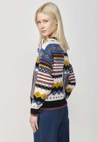 Cardigan en tricot avec un motif géométrique multicolore dans des teintes de bleu, jaune, rouge et noir, et des poignets et un ourlet côtelés.