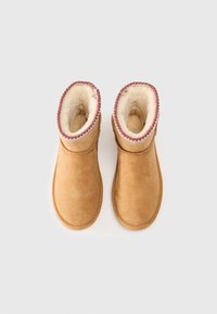 Bottines en daim beige avec une doublure en fausse fourrure douce et un bord décoratif rose en haut de l'ouverture. Texture lisse, design simple.