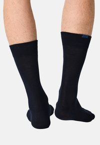 Marineblå bomuldsstrømper med ribbet kant. Blød tekstur og længde til midt på læggen. Har et minimalistisk design med en lille blå accent.