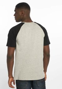 Grå og svart raglan t-skjorte; korte ermer, rund hals, mykt stoff, flate sømmer, kontrasterende ermefarge, avslappet passform.