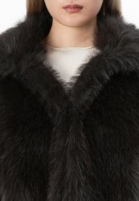 Abrigo de pelo oscuro con una textura gruesa y suave, y un cuello ancho. Presenta un escote en forma de V, mostrando la apariencia lujosa de la prenda.