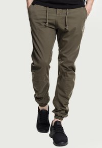 Pantalones cargo verde olivo con puños elásticos y cintura con cordón, fabricados en tejido ligero, combinados con zapatillas deportivas negras.