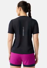 Camisa atlética de manga corta negra con tejido texturizado y logo reflectante "BROOKS" centrado en la parte posterior, combinada con pantalones cortos rosas.