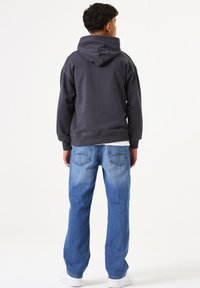 Sudadera gris oscura con un ajuste relajado, que cuenta con un gran bolsillo trasero y una capucha con cordón, combinada con pantalones vaqueros de un azul claro y zapatillas blancas.