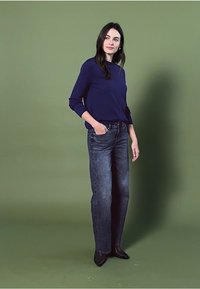 Granatowa bluzka z długim rękawem zestawiona z ciemnoniebieskimi dżinsami. Dżinsy mają prosty krój, natomiast bluzka ma okrągły dekolt i luźny krój.
