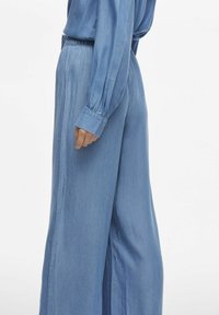 Pantaloni azzurro chiaro a gamba larga realizzati in un tessuto morbido, con vita elasticizzata e polsini arricciati. Taglio fluido con texture liscia e senza motivi visibili.