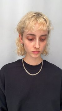 Srebrny naszyjnik z siateczki noszony na czarnej koszuli, w zestawieniu z okrągłymi srebrnymi kolczykami. Osoba ma jasne, falowane włosy i jasną cerę.