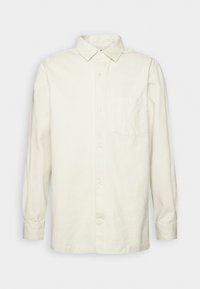 Chemise crème à manches longues, boutonnée, avec col et poche poitrine, posée à plat sur un fond blanc.