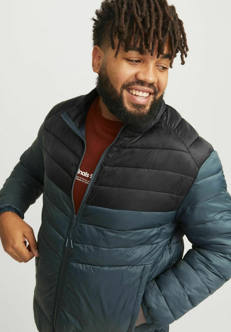 Chaqueta acolchada en colores bloque de azul oscuro y negro, con cierre de cremallera, cuello alto y textura suave y brillante.