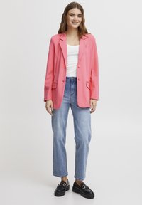 Rozā žakete ar pielāgotu dizainu, divām pogām un priekšējiem kabatām, pārī ar gaiši ziliem straight-leg džinsiem un melniem platformas loafers.